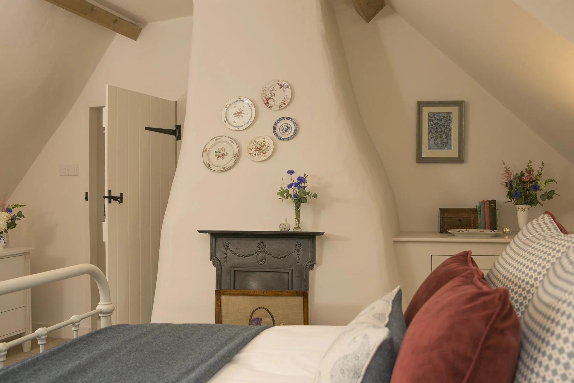 Curved plastered chimney breast with restored cast-iron fire grate, embroidered fire screen and antique plates